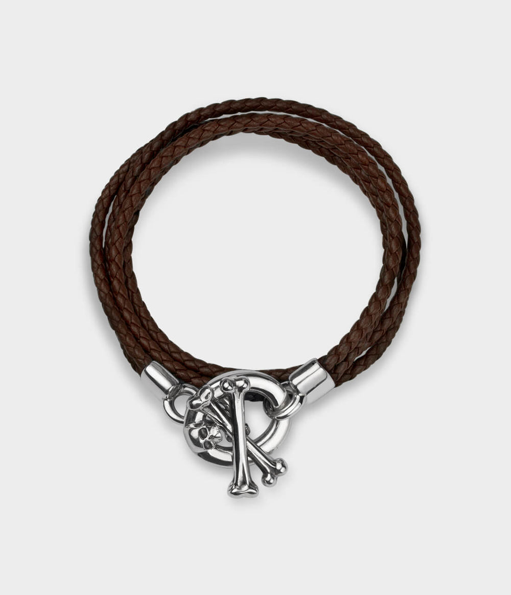 A view from above of a brown leather double strand bracelet with a detailed silver skull and crossbone T bar catch.