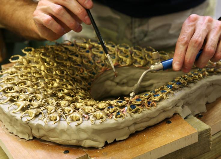 Craftsman soldering the gold stag beetle collar for Snow White and the Huntsman, bedded in clay on the bench