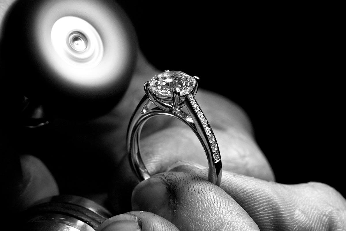 Black and white close-up of a diamond solitaire engagement ring with diamond set shoulders held in the workshop