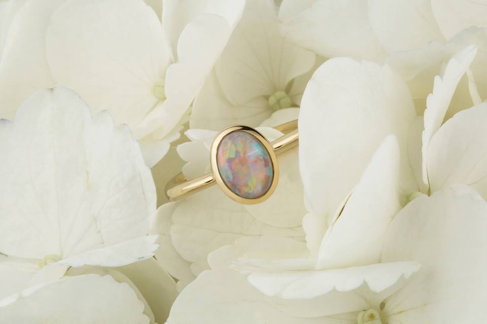 Yellow gold ring set with an oval opal in a bezel, resting on white hydrangea petals