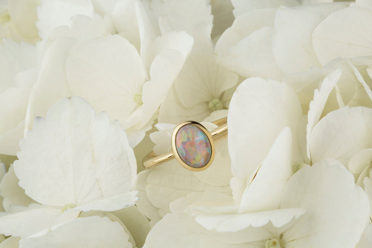 Yellow gold ring set with an oval opal, resting among white hydrangea petals
