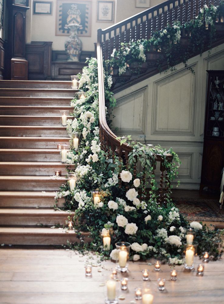 Grand wooden staircase garlanded with white roses, greenery and candles for a wedding