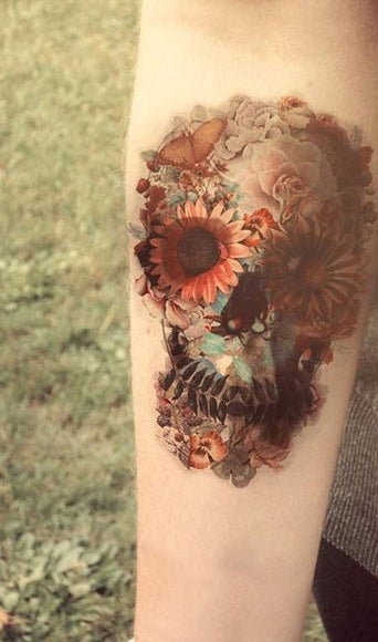 Colour tattoo on a forearm of a skull made from sunflowers, roses, leaves and a butterfly