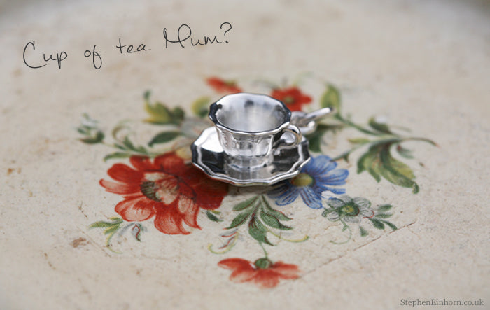Silver teacup and saucer charm on a floral painted tray, with a handwritten Cup of tea Mum caption