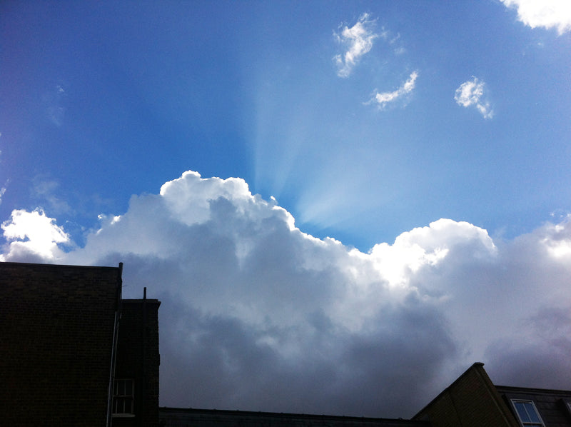 Sunlight streaming from behind a white cloud over London rooftops against a blue sky