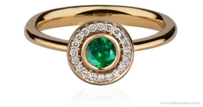 Yellow gold ring with a round emerald in a bezel, surrounded by a halo of small white diamonds