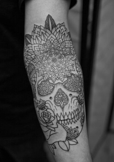 Forearm tattoo of a skull with geometric mandala flowers and a rose, drawn in fine black linework