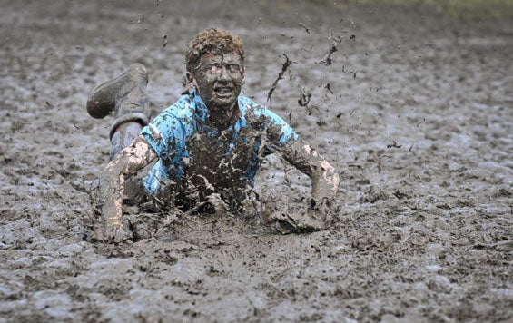 Festival-goer in a blue shirt sliding through deep mud at a rain-soaked Glastonbury Festival
