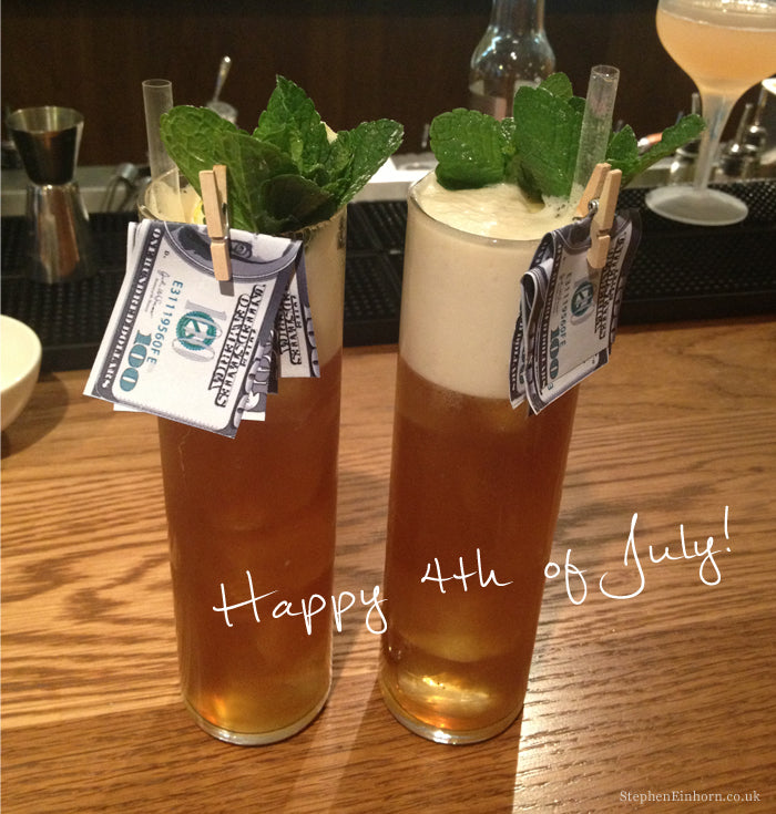 Two tall iced cocktails with mint garnish and pegged dollar bills on a bar, captioned Happy 4th of July