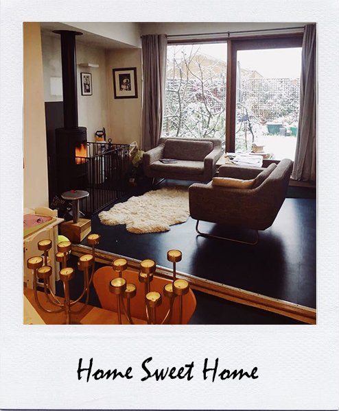 Polaroid-style photo of a living room with a wood burner, grey armchairs and snowy garden, captioned Home Sweet Home