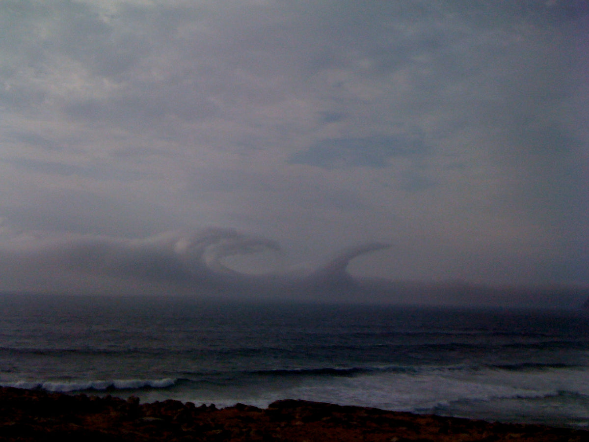 Wave-shaped clouds curling over a grey sea above a rocky shoreline