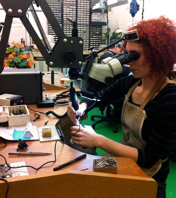 Jeweller with red curly hair using a microscope to work on a diamond ring at the bench in our London workshop