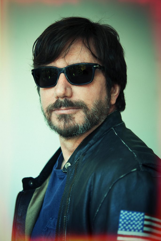 Portrait of photographer JP Masclet in dark sunglasses and a black leather jacket with an American flag patch