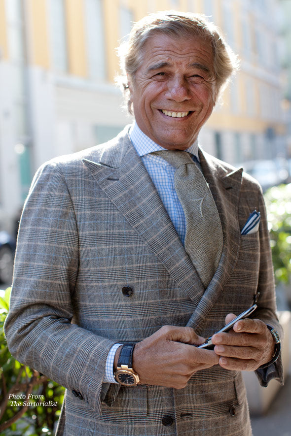 Smiling older man in a grey check double-breasted suit and tie, wearing a gold watch on a leather strap