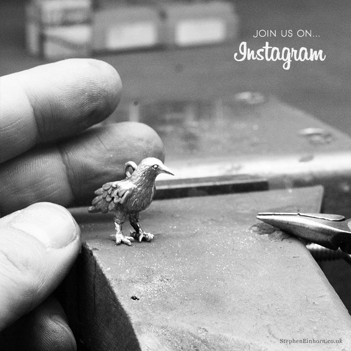 Silver crow charm standing on a jeweller's bench beside fingers and pliers, with a Join us on Instagram caption