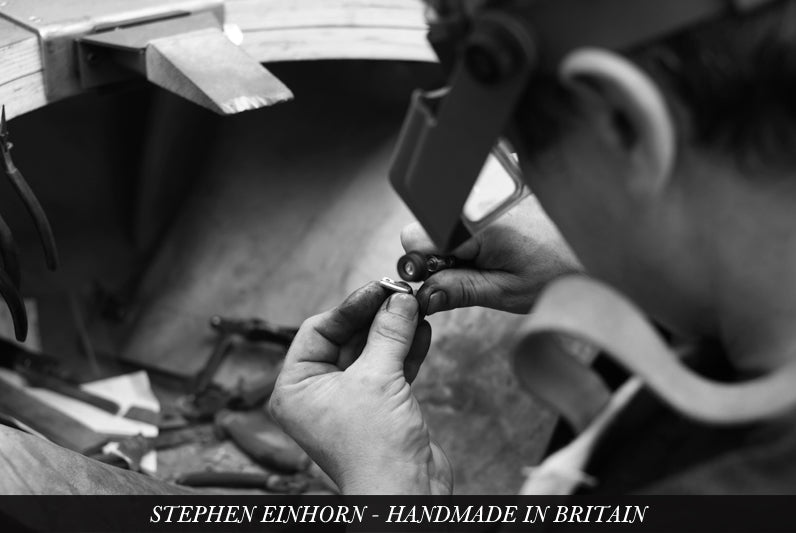Jeweller wearing a head loupe works on a small silver piece at the bench, captioned Handmade in Britain