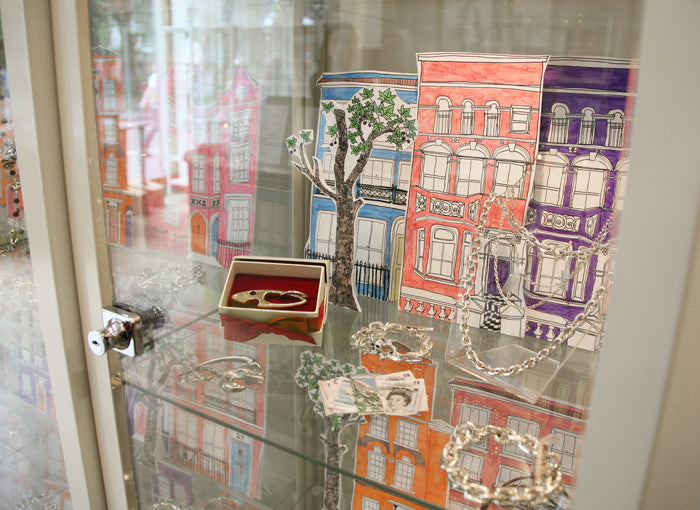 Silver bracelets and chains in our shop display case, in front of hand-painted London house facades