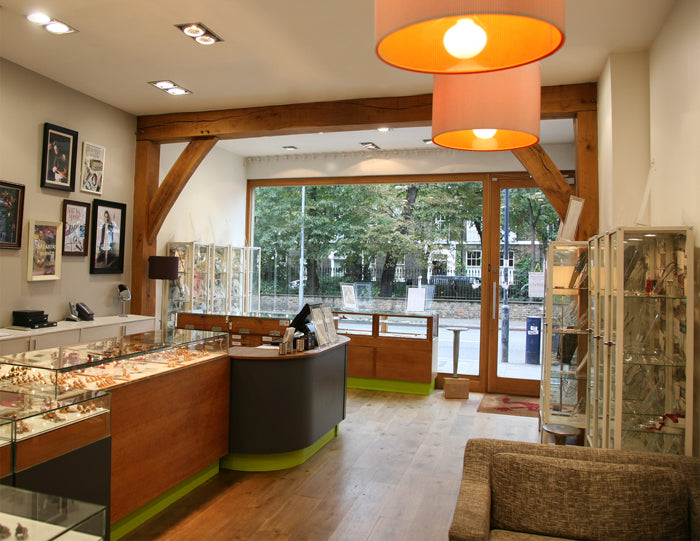 Our London shop interior with glass jewellery cabinets, oak beams, orange pendant lights and a view onto the street