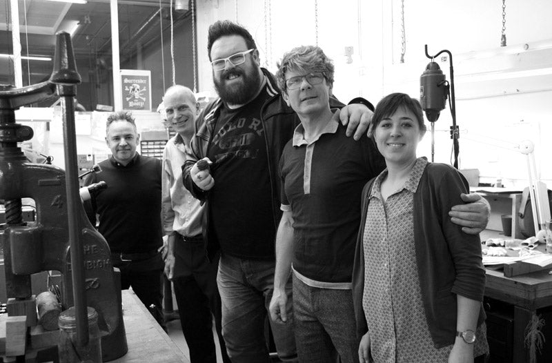 Kristian Nairn with the Stephen Einhorn team beside a press in the London workshop, black and white
