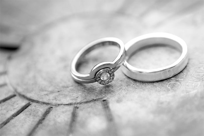 Black and white close-up of a diamond engagement ring and a plain wedding band resting on a stone surface