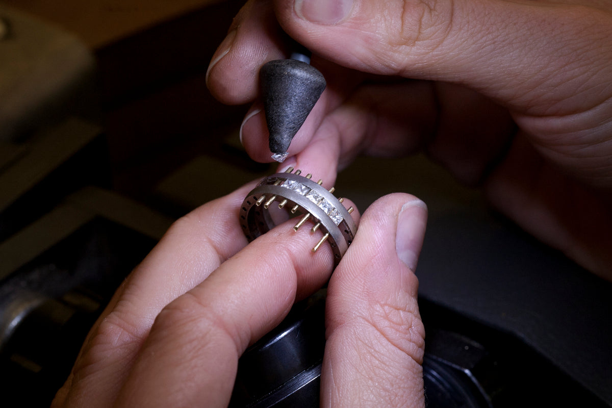 Jeweller's hands holding a ring band with stones in their claws while setting the Geo Elipse eternity ring