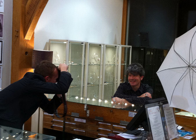 Photographer shooting Stephen Einhorn as he leans on a jewellery counter in the shop, beside a white umbrella light