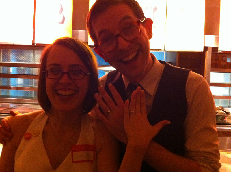 Newly married couple in glasses smiling and holding up their hands to show their wedding rings