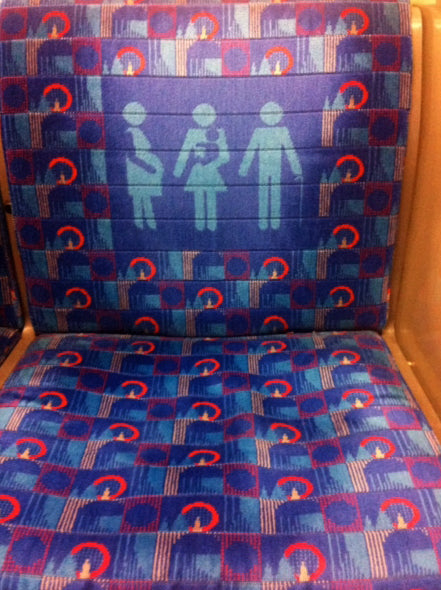 London Underground seat with blue and red patterned fabric and priority seat figures woven into the back