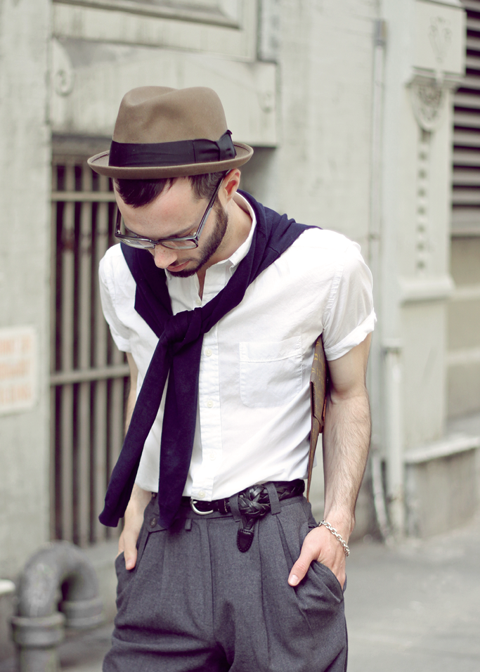 Man in a trilby, white shirt and navy jumper over his shoulders wearing a silver chain bracelet