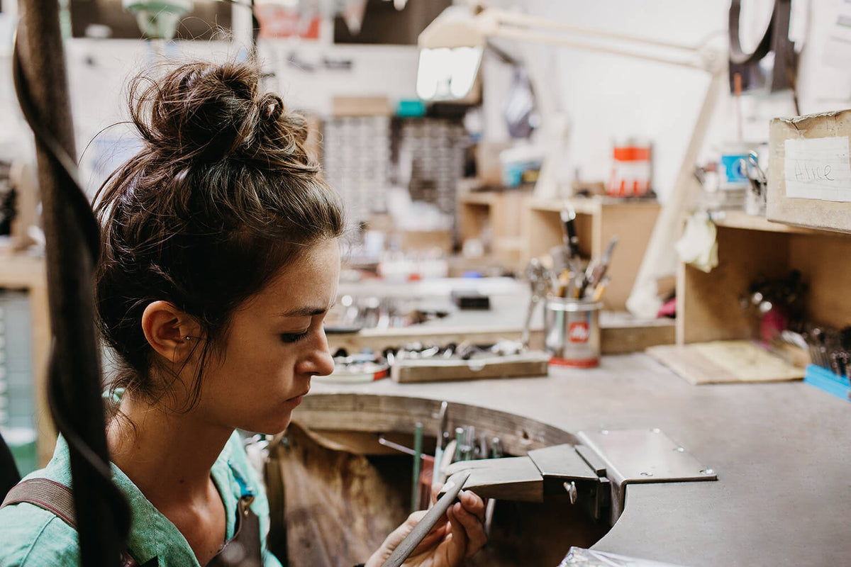 Jeweller with her hair tied up working at a wooden bench in our Islington workshop
