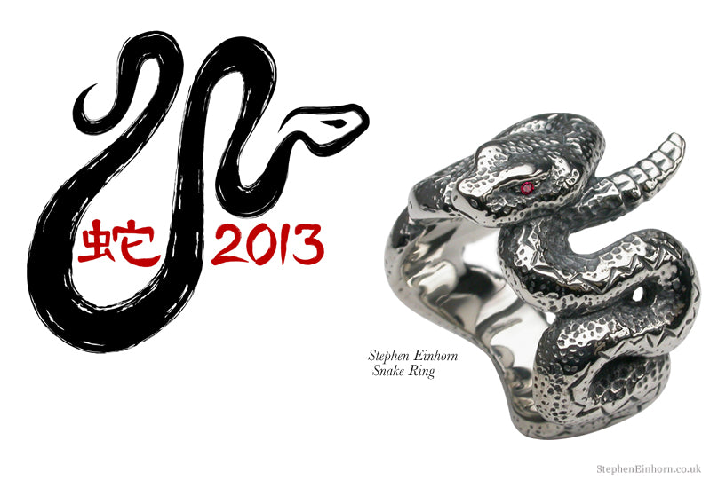 Silver snake ring with a coiled textured body and red stone eye, beside a brush-drawn snake and 2013 in red