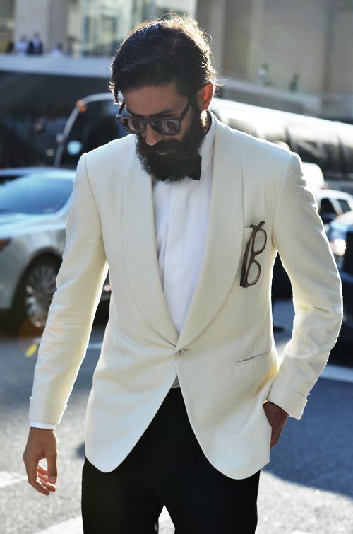 Bearded man in sunglasses, a cream shawl-collar dinner jacket and black bow tie on a city street