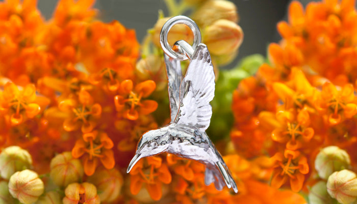Fairtrade silver hummingbird charm on a jump ring, shown against bright orange flowers