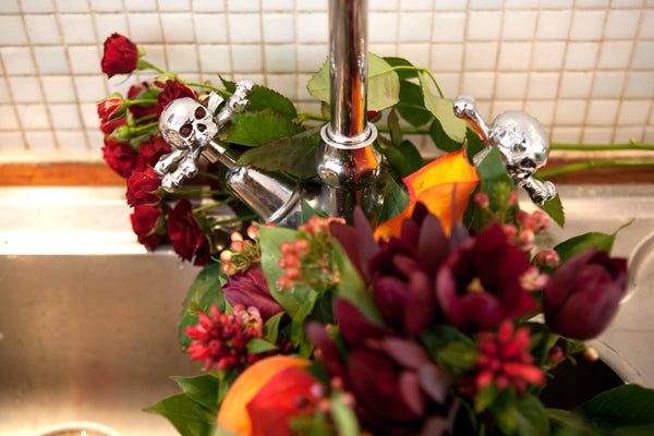 Wedding bouquet of red roses and dahlias in a sink with silver skull-shaped tap handles