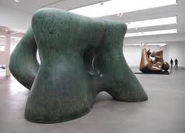 Large green bronze abstract sculpture in a white gallery, with a second bronze figure behind