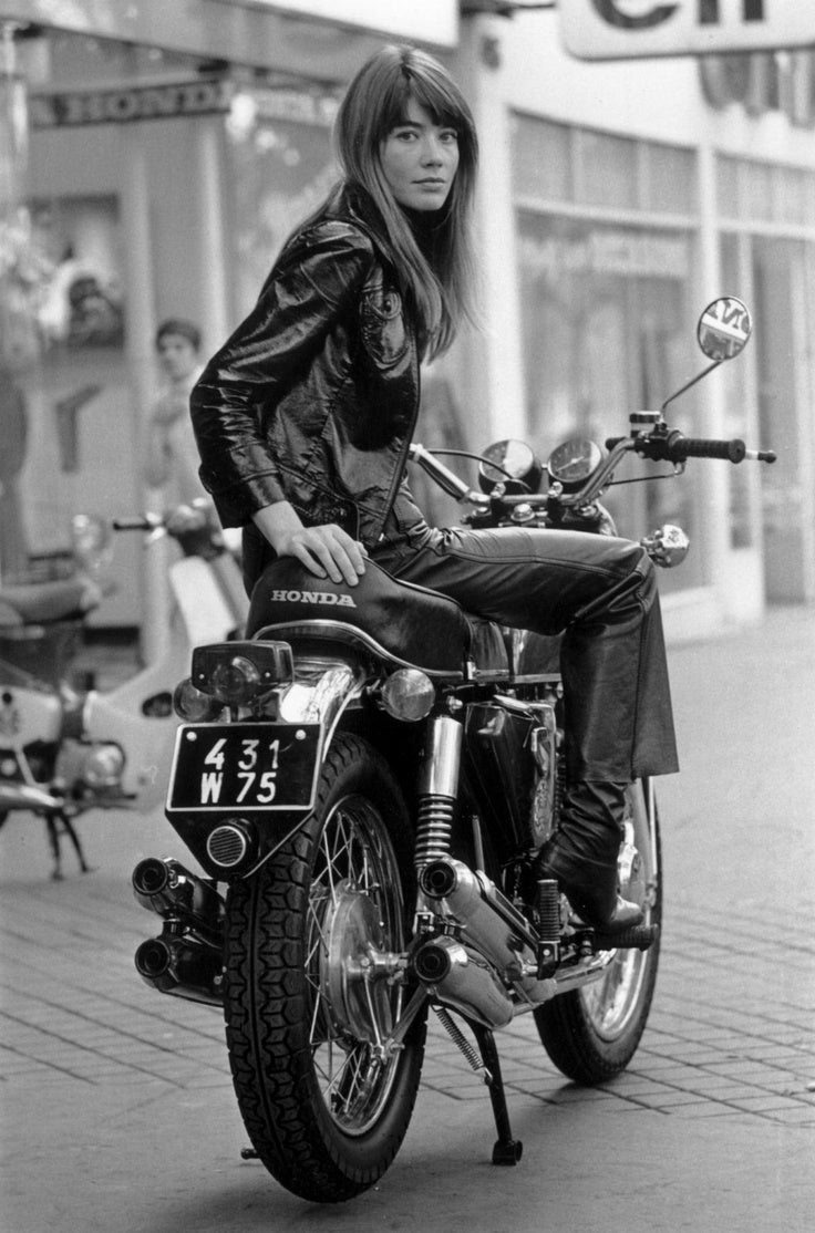 Woman in a leather jacket and trousers sitting on a Honda motorbike in a Paris street, black and white
