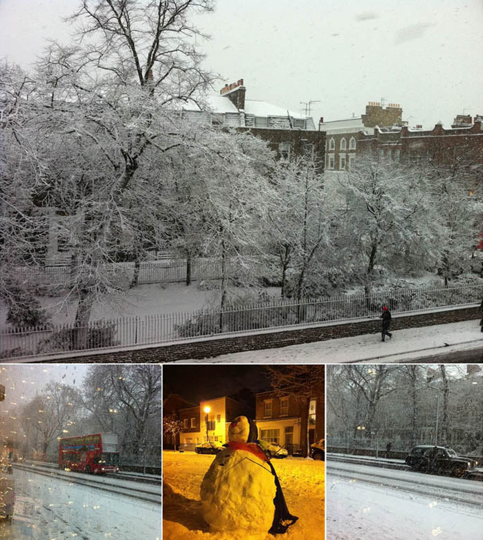 London street and garden square under heavy snow, with a red bus and a snowman in lamplight