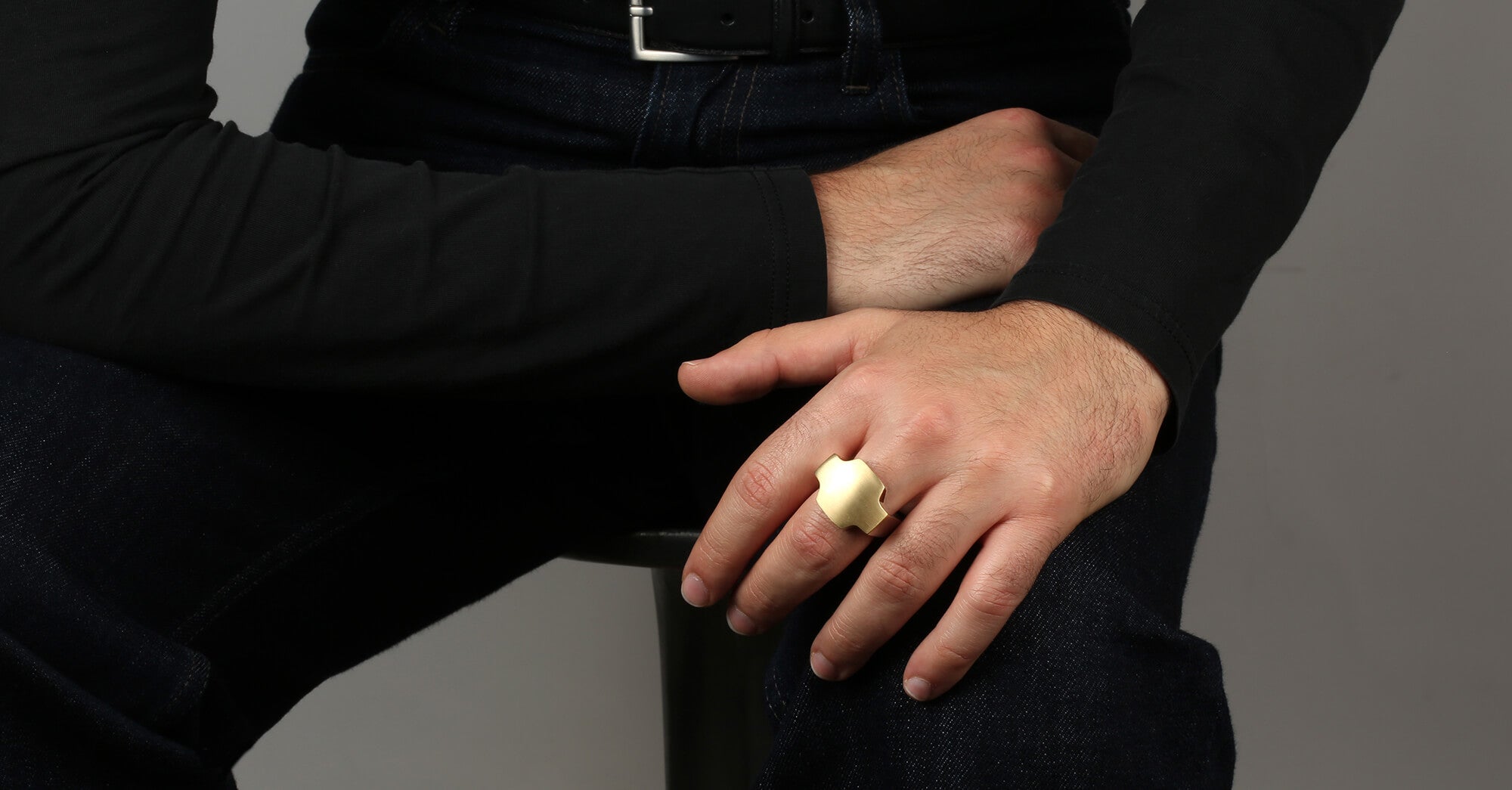 Person wearing a black outfit with a ring on a grey background