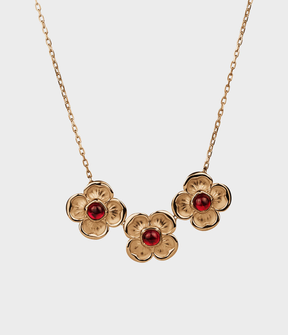 A yellow-gold necklace on a delicate chain with three four-petal flowers, each one holding a red ruby