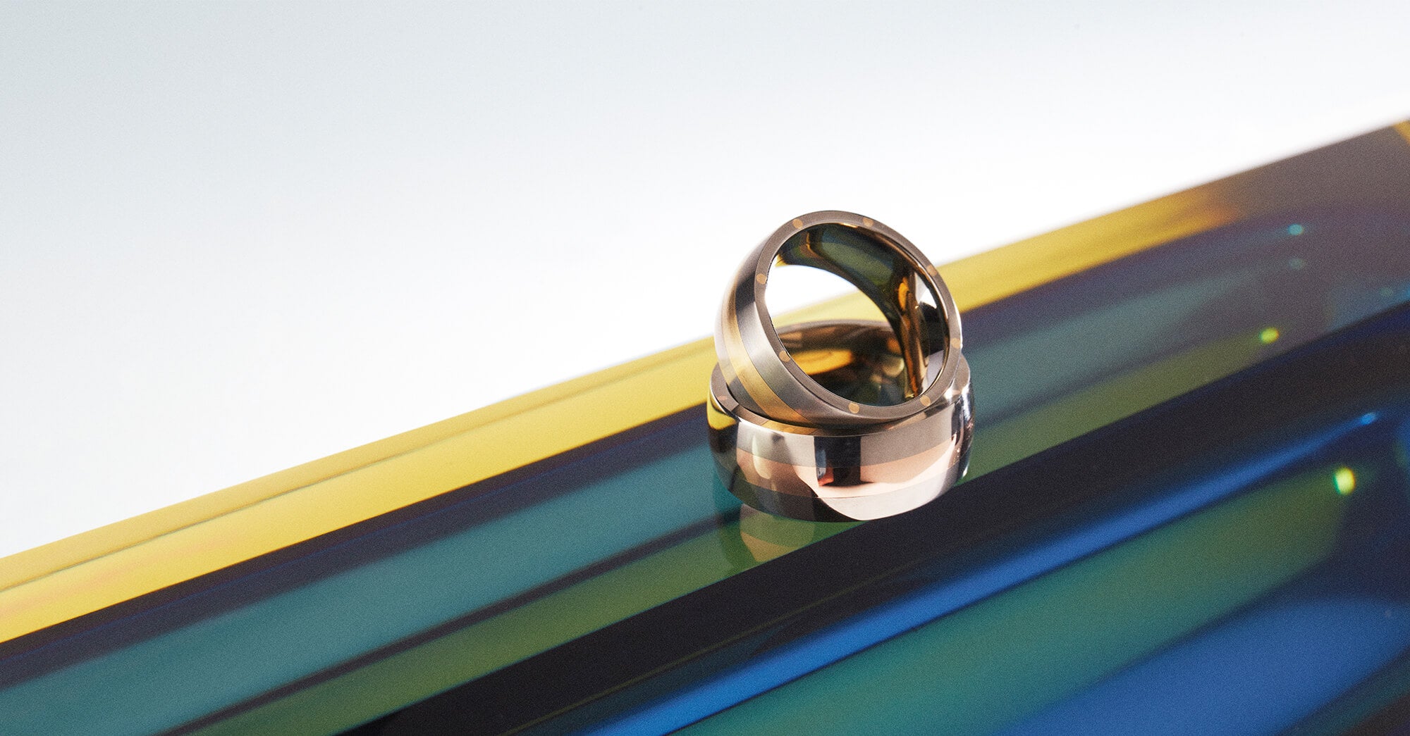 Two mixed metal precious gold and titanium rings photographed on a green blue and yellow striped background