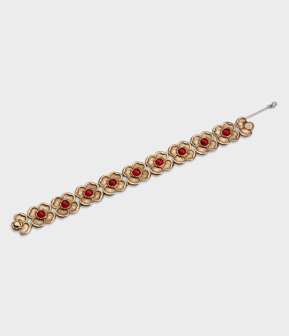 Yellow-gold ornate bracelet with interlinking flowers, each inset with a red ruby laying flat on a table with a magnetic clasp and delicate silver safety chain