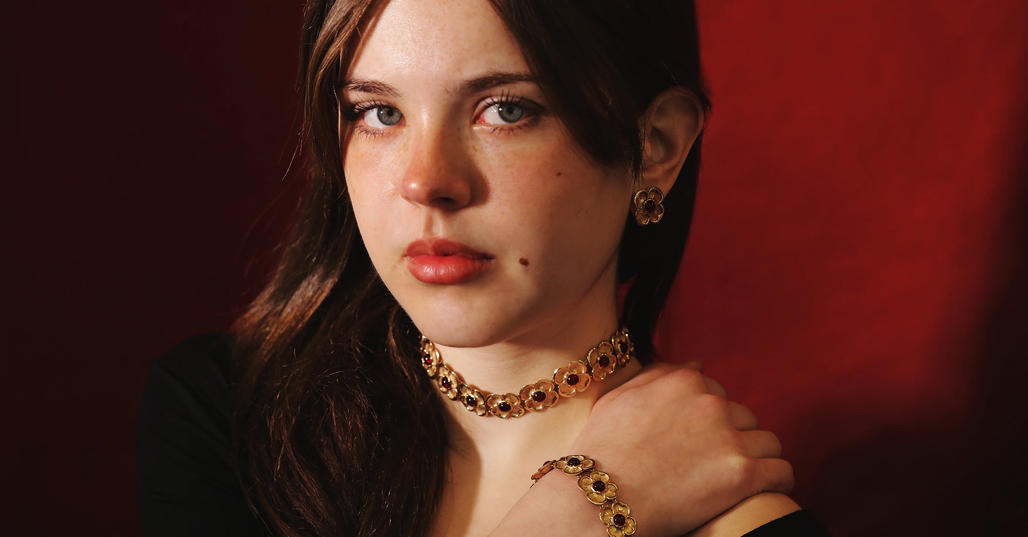 pretty young woman wearing a flowered choker, bracelet and earrings on a dark red background