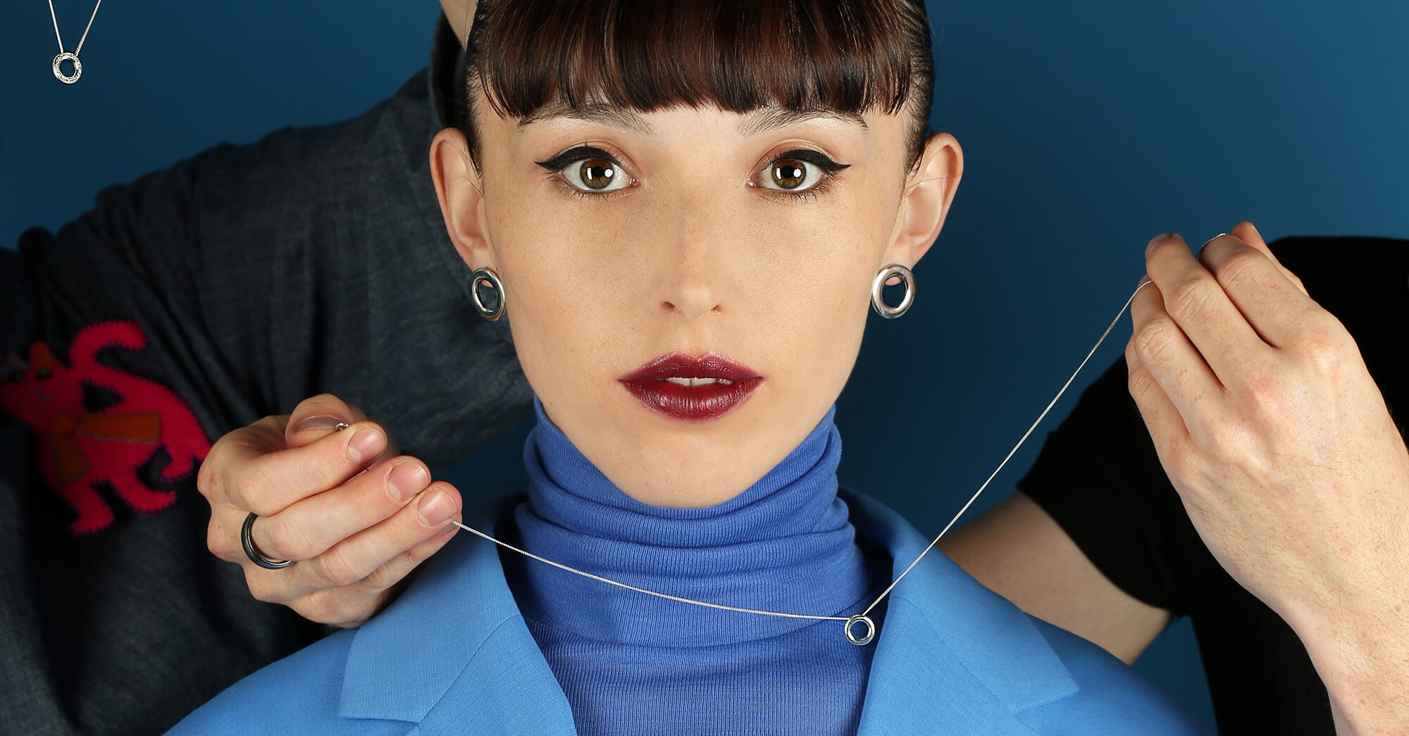 Head and shoulders close up of woman wearing silver earrings with brown eyes dark hair and blue clothes