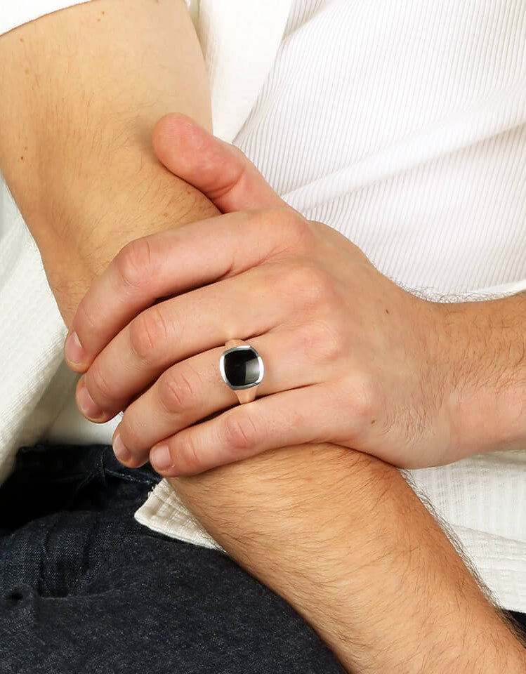A close up of a man's hand wearing a silver inlaid signet ring with onyx