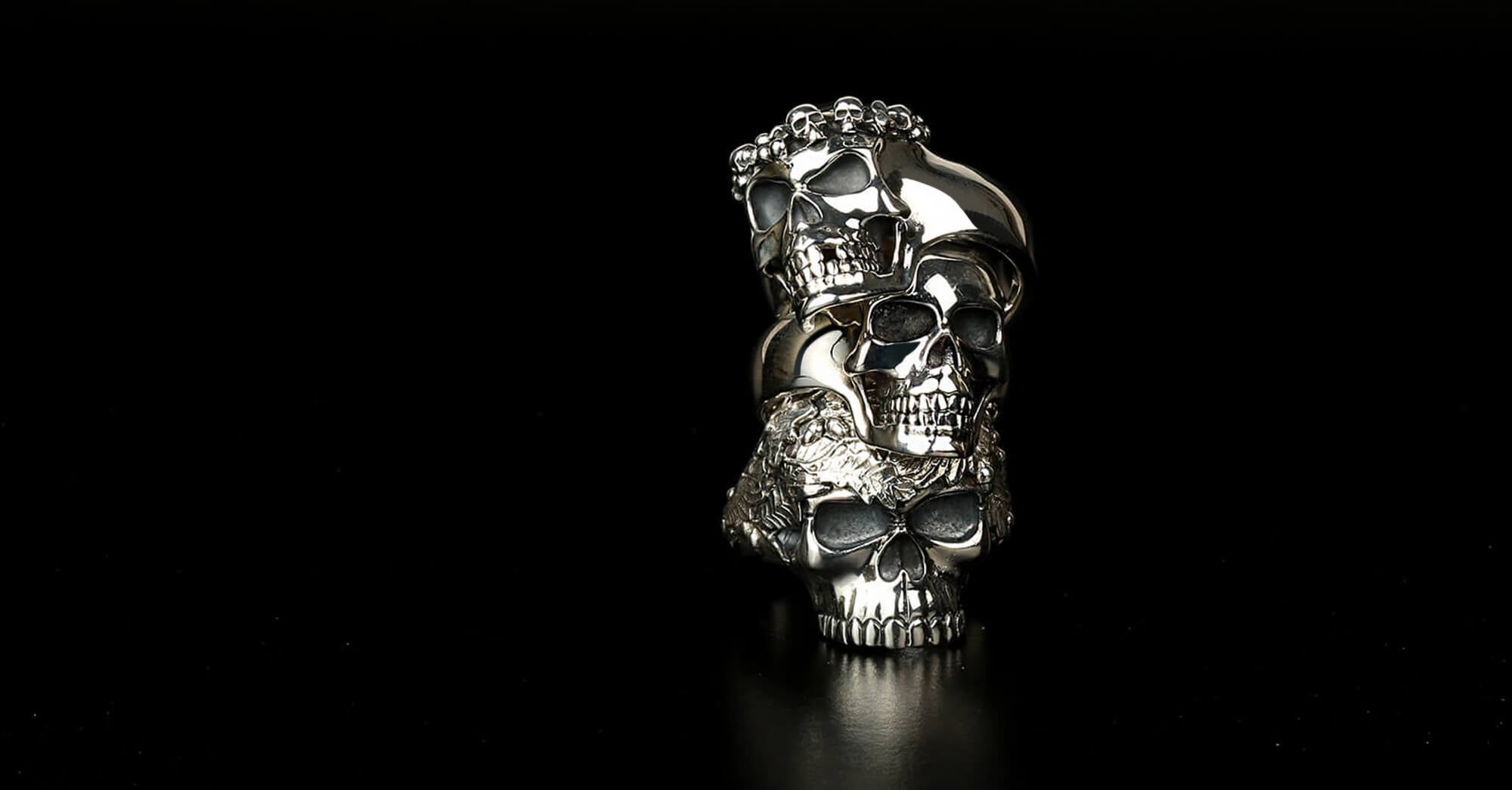 A man's hand wearing a black and silver bracelet and three skull rings on his fingers.