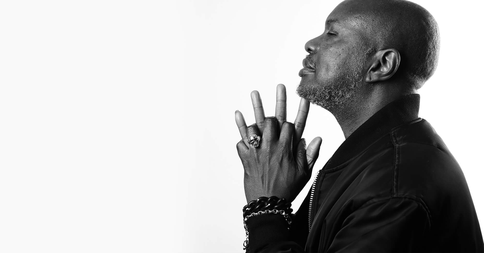 A man's hand wearing a black and silver bracelet and three skull rings on his fingers.