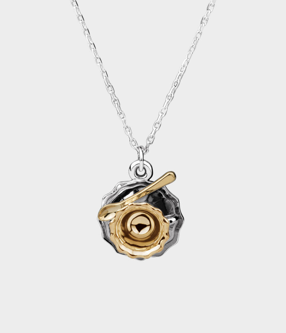 front view of a silver and yellow gold teacup on a silver chain.