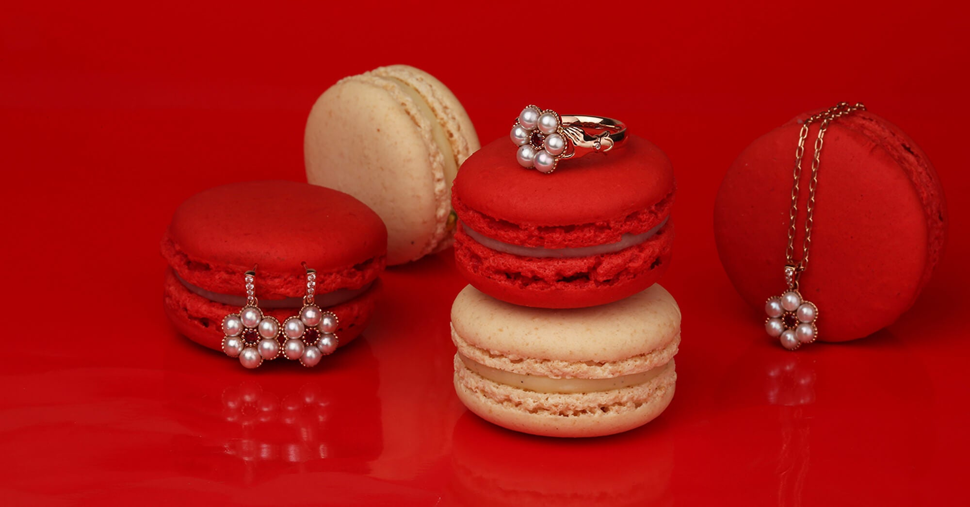 Red and beige macarons with pearl, ruby and gold jewellery on a red background.