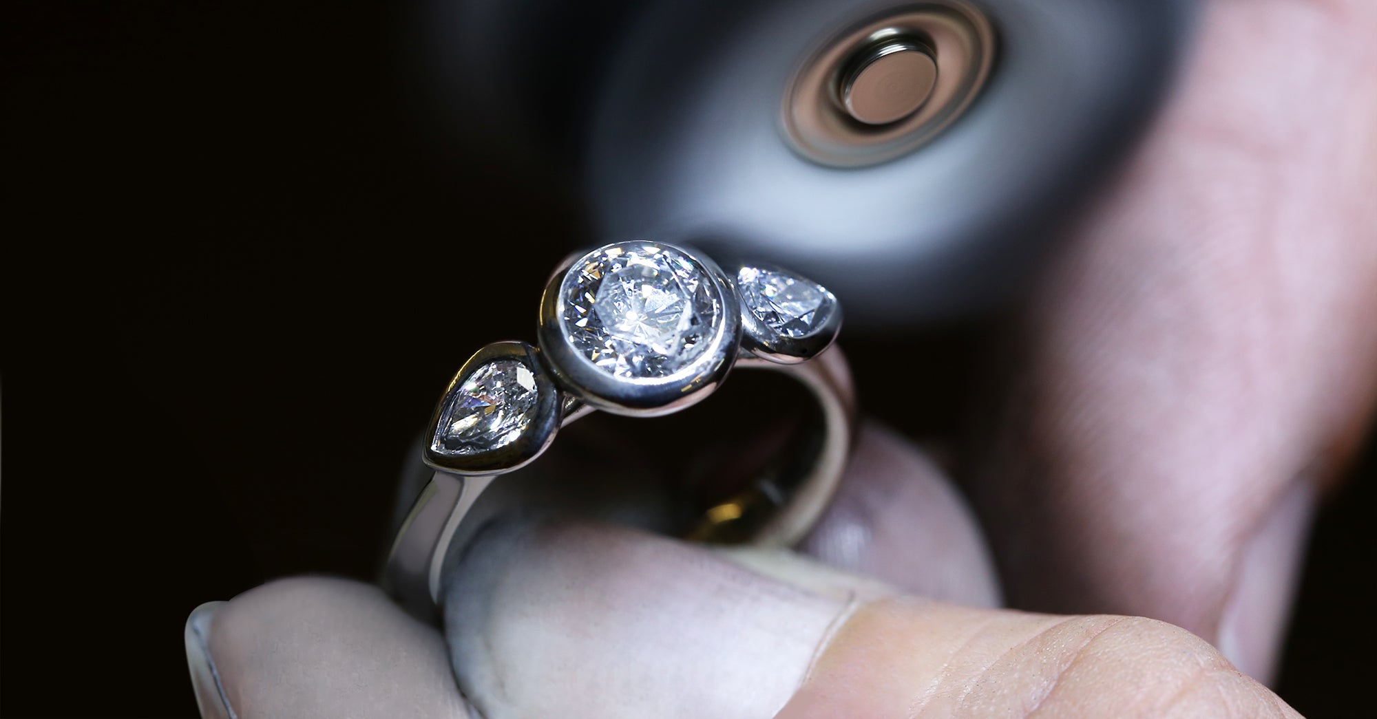 A workshop picture picture showing a diamond Angel ring being polished. The ring cosists of a round brilliant cut diamond and two pear shaped diamonds on either side.