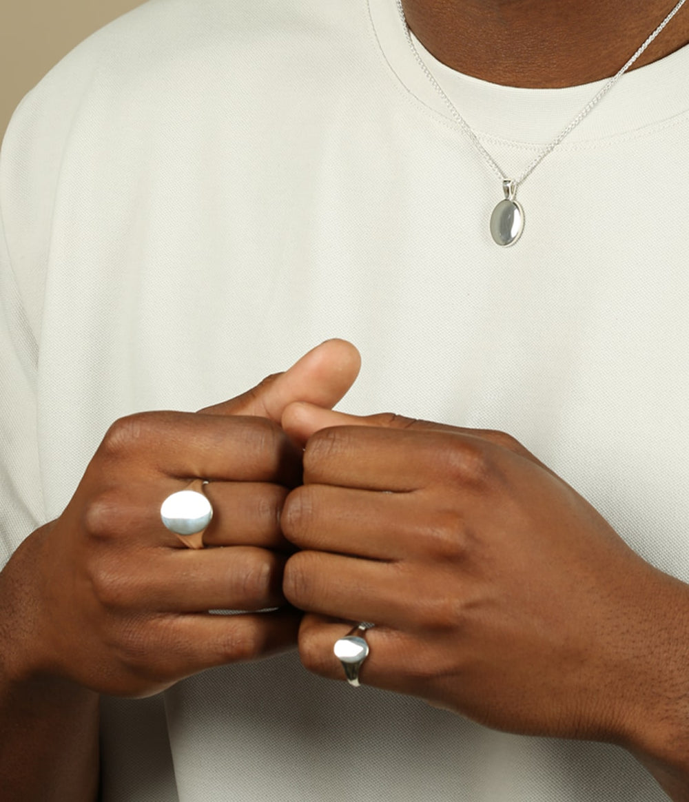 a man in a white tshirt wearing the oval signet pendant in silver and wearing two oval signet rings one large and one small.